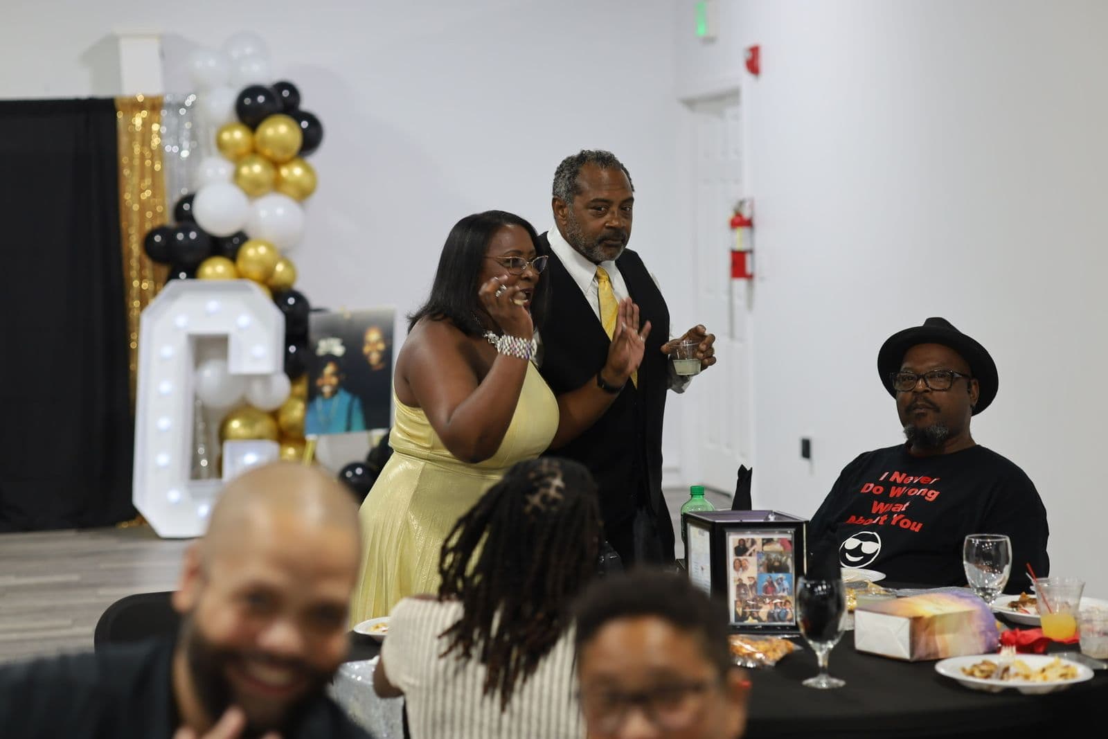 Host in a gold gown addressing the room